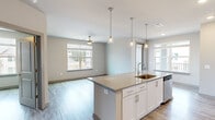 Located in Suwanee, GA, this thoughtfully designed 2-bedroom, 2-bathroom residence offers a clean, modern aesthetic with a cohesive neutral palette and wood-look flooring throughout. The open-concept layout connects the kitchen, dining, and living areas seamlessly, creating a bright and functional living space. The kitchen is a standout feature, showcasing white shaker-style cabinetry, granite countertops, a large center island with a built-in sink, stainless steel appliances including a refrigerator, range, and microwave, and stylish pendant lighting overhead. Natural light pours in through multiple windows, and ceiling fans in the main living area and bedrooms add both comfort and style. The primary bedroom is generously sized, featuring dual windows with exterior views, a ceiling fan, and access to a well-appointed en-suite bathroom. The primary bath includes a granite-topped vanity with white cabinetry, a glass-enclosed shower, and a walk-in closet with wire shelving. The second bedroom is bright and airy with its own ceiling fan and natural light. The second bathroom features a tub-shower combo, granite vanity, and matching wood-look flooring. A hallway connects the living spaces to the bedrooms, and two dedicated closets provide ample storage throughout.