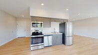 Located at 1620 N River Ridge Blvd, Unit B306, in Spokane, WA, this thoughtfully designed single-floor unit offers a clean, contemporary aesthetic throughout. The open-concept living and kitchen area is anchored by warm light hardwood flooring that extends seamlessly across the space, creating a bright and cohesive feel.

The kitchen is outfitted with a full suite of stainless steel appliances, including an electric range, over-the-range microwave, dishwasher, and a French door refrigerator. Gray shaker-style cabinetry with modern hardware provides ample storage, while white countertops and recessed lighting contribute to the crisp, modern finish.

The living area is generously sized and bathed in natural light from a bank of large windows fitted with blinds, offering views of surrounding greenery. A wall-mounted mini-split heating and cooling unit ensures year-round comfort. A sliding glass door provides additional light and outdoor access.

The bathroom is well-appointed with a gray shaker vanity, white countertop, a large mirror, and a shower/tub combination, all finished in a clean, neutral palette consistent with the rest of the unit. Recessed lighting and light hardwood flooring complete the space with a polished touch.