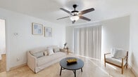 This efficiently designed single-floor residence offers a thoughtful layout across one bedroom, one bathroom, a combined living/dining/kitchen area, and a closet. The living room is bright and airy, featuring light travertine tile flooring, a ceiling fan with light fixture, and a large sliding glass door dressed with vertical blinds that allows abundant natural light to fill the space. The room's clean white walls and minimalist aesthetic create a calm, open atmosphere. The kitchen is positioned adjacent to the living and dining area and features granite countertops with a breakfast bar overhang, stainless steel appliances including a refrigerator and wall oven, and eye-catching pendant lighting in a warm amber tone that adds a distinctive design element. The bedroom offers warm hardwood-style flooring, a ceiling fan, a window with blinds, and direct access to both a closet and the bathroom. A built-in desk area provides functional workspace within the room. The bathroom is clean and straightforward, featuring a full tub-shower combo with white tile surround and classic fixtures. Overall, the space presents a cohesive, light-toned interior that maximizes functionality within a compact footprint.