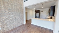 This two-story Frisco residence blends contemporary design with functional living across two well-appointed levels. The main floor makes an immediate impression with a dramatic exposed brick accent wall soaring toward the upper level, complemented by warm wood-look flooring that flows consistently throughout the home. The kitchen is a standout feature, equipped with dark espresso cabinetry extending to the ceiling, stainless steel appliances including a French door refrigerator, granite-style countertops, a mosaic tile backsplash, a built-in wine cooler, and a kitchen island with an undermount sink illuminated by sleek pendant lights. The main living area benefits from tall ceilings and abundant natural light from large windows. A clean entryway with recessed lighting provides a welcoming arrival point. Upstairs, an open hallway with black metal railing overlooks the lower level, enhancing the sense of vertical space. The upper floor includes well-sized bedrooms with ceiling fans, natural light, and closet access. Bathrooms feature dark vanity cabinetry, granite-style countertops, large mirrors, and tiled tub-shower combinations, maintaining a cohesive and polished aesthetic throughout the home.