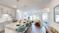 This well-designed single-story residence offers 2 bedrooms and 3 bathrooms within a thoughtfully organized floor plan. The open-concept layout connects the kitchen and living room seamlessly, creating a bright and functional common area. The kitchen features gray shaker-style cabinetry, granite countertops, a full suite of stainless steel appliances including a refrigerator, range, microwave, and dishwasher, along with a peninsula with bar seating illuminated by pendant lighting. Wood-style flooring runs throughout the main living areas, while the living room offers a ceiling fan, natural light from multiple windows, and a door providing outdoor access. The primary bedroom is carpeted, features a ceiling fan, multiple windows, and connects to a walk-in closet with wire shelving. The second bedroom is similarly finished with carpet and natural light. The three bathrooms are fitted with granite-topped vanities and wood-style flooring. A dedicated laundry room houses a full-size top-load washer and dryer with overhead wire shelving. The overall aesthetic is clean and contemporary, with white walls and modern finishes throughout.