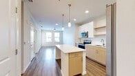 This well-appointed single-floor residence showcases a thoughtfully designed open-concept layout that seamlessly connects the kitchen and living areas. The kitchen is a standout feature, equipped with stainless steel appliances including a range, microwave, refrigerator with ice maker, and dishwasher. Light wood cabinetry paired with white upper cabinets and a classic subway tile backsplash create a clean, contemporary aesthetic. A central island with a white quartz-style countertop offers additional prep space and is accented by elegant brass pendant lighting. Recessed lighting and durable hardwood-style flooring extend throughout the main living areas, enhancing the bright, airy atmosphere.

The living area benefits from natural light streaming through multiple windows and features a ceiling fan for added comfort. A glass-paned door leads to a private balcony, extending the living space outdoors. The bedrooms are generously sized, finished with plush carpeting, ceiling fans, and large windows that frame pleasant neighborhood views. The bathroom is finished with light wood vanity cabinetry, white countertops, subway-tiled tub surround, and hardwood-style flooring, maintaining the cohesive modern aesthetic found throughout the residence.