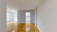 This well-proportioned three-bedroom, one-bathroom unit at 1284 Danforth Road offers a comfortable and practical layout across a single floor. The space is unified throughout by warm-toned parquet wood flooring in a classic basket-weave pattern, lending a timeless character to every room.

The living room is generously sized, featuring neutral grey walls, clean white baseboards, and a large window that fills the space with natural light and frames lush, tree-lined views. A radiator beneath the window provides efficient heating. The open feel of the room is enhanced by its bright, airy palette.

Each of the three bedrooms continues the parquet flooring theme. Two of the bedrooms feature windows overlooking greenery, paired with radiators, creating bright and comfortable retreats. The primary bedroom includes a double-door closet, offering practical built-in storage. A third bedroom also features a double closet and connects conveniently to the hallway.

The bathroom is finished with full-height pale yellow ceramic tile surrounding a full-sized soaking tub and shower combination, complemented by chrome fixtures and a wall-mounted medicine cabinet.

A central hallway connects all rooms efficiently, contributing to the unit's functional flow. The neutral tones, natural light, and consistent flooring throughout create a cohesive and inviting living environment.