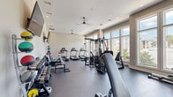 Located at 1125 Old Graves Mill Rd in Lynchburg, Virginia, this fitness center offers a comprehensive workout facility within a bright, well-designed single-level space. The room features neutral-toned walls, durable rubber flooring, and recessed lighting complemented by ceiling fans that maintain a comfortable environment during workouts.

Large windows along one wall flood the space with natural light and provide views of the surrounding outdoor scenery, creating an open and energizing atmosphere. The cardio section is equipped with multiple treadmills and a stationary cycling bike, ideal for sustained aerobic training. A multi-station cable machine serves as the centerpiece for strength and resistance training, accompanied by an adjustable workout bench suitable for a variety of exercises.

The free weights area includes a well-stocked dumbbell rack with a broad range of weights, a medicine ball tower with color-coded balls for functional training, and a step platform for aerobic and core exercises. Wall-mounted flat-screen televisions are positioned throughout the space for entertainment during workouts. A full-length mirror section enhances the sense of space and supports proper form during training. The fitness center is designed to support a wide range of fitness goals, from cardio endurance to strength building, making it a versatile and fully functional facility.