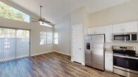 This single-floor home is designed with an open, airy layout that maximizes both comfort and functionality. Vaulted ceilings soar throughout the main living and kitchen areas, creating an impressive sense of vertical space and volume. Rich wood-look flooring extends seamlessly across every room, providing a warm and cohesive aesthetic.

The kitchen is a standout feature, outfitted with a full suite of stainless steel appliances including a side-by-side refrigerator with in-door ice and water, a range with oven, an over-the-range microwave, and a dishwasher. Crisp white shaker-style cabinetry lines the walls from floor to ceiling, complemented by light neutral countertops and a double-basin sink positioned beneath a window for natural light.

The living area is generously proportioned and bathed in natural light, thanks to large sliding glass doors and elevated clerestory windows that draw in sunlight from multiple angles. A ceiling fan serves both the living and dining areas, enhancing airflow and comfort. A dedicated bedroom includes a well-appointed walk-in closet with built-in shelving and hanging rods, providing ample storage. Throughout the space, neutral warm-toned walls, clean white trim, and recessed lighting contribute to a fresh, move-in-ready atmosphere.