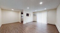 Located at 46 Camp St in Middletown, Connecticut, this single-floor unit offers a clean, modern living experience with thoughtfully updated finishes throughout. The open living area is bright and welcoming, featuring warm wood-look plank flooring, recessed lighting, and a large sliding door with vertical blinds that allows natural light to fill the space. A wall-mounted air conditioning unit and baseboard heating ensure year-round comfort. A convenient pass-through window connects the living area to the kitchen, adding an open, airy feel. The kitchen is well-appointed with rich dark cabinetry, sleek quartz countertops with subtle veining, a subway tile backsplash, and stainless steel appliances including a refrigerator and electric range. The bedroom areas feature the same wood-look flooring, recessed lighting, and ample closet space, providing a calm and functional retreat. The bathroom is a standout, showcasing floor-to-ceiling marble-look tile in the tub surround, accented by a decorative mosaic tile border, complemented by dark slate-style floor tiles and a clean white vanity. Natural light filters in through a slatted window, completing this polished space.