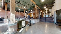 Located at 1218 Izard Street in Omaha's vibrant downtown, this single-floor commercial space masterfully blends historic industrial character with contemporary design. The interior retains its original exposed brick walls, heavy timber columns, and wood beam ceilings, all complemented by polished concrete and warm hardwood flooring throughout. Soaring ceilings with exposed ductwork and teal-painted mechanical systems add an authentic industrial aesthetic, while globe pendant lighting creates a warm, inviting ambiance.

The layout is thoughtfully organized to serve a variety of work and collaboration needs. A welcoming reception and lounge area greets visitors near the front entry, featuring plush seating and a fireplace set against a striking honeycomb wood-clad accent wall. Multiple glass-walled conference and private office rooms line the corridors, offering visual transparency while maintaining acoustic separation. A raised lounge zone with booth-style seating and patterned carpet provides a comfortable social hub.

Two hallways guide occupants through the space, connecting distinct zones seamlessly. Natural light filters in through front-facing windows, brightening the polished concrete entryway. The overall ambiance is one of refined industrial sophistication — a well-preserved historic shell transformed into a dynamic, functional, and design-forward professional environment.