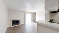 This single-floor residence is organized into a practical, open layout that connects the main living areas seamlessly. The living room serves as the focal point of the space, highlighted by a tile-surround fireplace that anchors the room with a classic touch. Wood-look plank flooring extends throughout the living area, adding warmth and visual continuity. A large sliding glass door dressed with vertical blinds fills the room with natural light and provides access to the exterior. The textured ceiling is consistent throughout the unit.

The kitchen is positioned adjacent to the living room in an open-concept arrangement, featuring a raised countertop with a speckled surface, black electric range with overhead ventilation, and a black refrigerator. The hard-surface flooring continues into the kitchen and a connected utility area.

The bedrooms are carpeted for comfort, each featuring neutral walls, a window with horizontal blinds admitting natural light, and convenient access to the hallway. The bathroom is equipped with a full tub-shower combination featuring white tile surround and chrome fixtures, paired with wood-look flooring and clean, neutral finishes throughout.