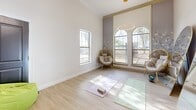 Located at 3303 Southern Oaks Blvd in Dallas, TX, this thoughtfully designed wellness studio offers a calm and inviting atmosphere well-suited for yoga, fitness, or mindfulness activities. The single-room space is bathed in natural light streaming through a striking pair of arched windows, complemented by an additional standard window that brightens the open floor area throughout the day.

The interior features light wood-tone flooring that lends warmth and a clean aesthetic, while crisp white walls create an airy, expansive feel. A decorative floral mural panel adds an elegant botanical accent, enhancing the room's tranquil ambiance. Crown molding and high ceilings contribute to the sense of vertical openness, and a modern circular ring pendant light serves as both a functional and stylish focal point overhead.

Two full-length arched mirrors with gold and neutral frames are positioned to amplify natural light and provide visual feedback during practice sessions. A pair of woven rattan egg chairs offer comfortable seating options, while yoga mats, blocks, and a kettlebell signal the studio's active-use purpose. Additional amenities include a rolling supply cart, bean bag seating for relaxation, and a dark double-door entry that anchors the space with a bold contrast. This studio blends practicality with refined design to create a welcoming environment for movement and wellness.