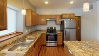 This single-floor residence offers a functional and comfortable layout designed for everyday living. The kitchen serves as a standout feature, showcasing warm oak cabinetry, granite-look countertops, stainless steel appliances including a refrigerator, range, and dishwasher, and a central island with pendant lighting overhead. Rich hardwood-style flooring extends through the kitchen and into the open living area, which is brightened by recessed lighting and a window that draws in natural light.

The bedrooms are finished with plush carpeting and neutral tones, providing a calm and restful atmosphere. One bedroom features a walk-in closet with built-in shelving and direct access to an adjacent room, offering added versatility. Windows throughout the bedrooms frame outdoor views and allow for ample daylight.

The bathroom is clean and simply appointed, with a full tub-shower surround, a wood-trimmed vanity, and access to a closet with wire shelving. A dedicated laundry area houses a full-size washer and dryer, adding significant convenience to the home.

Consistent warm wood trim, neutral wall tones, and durable flooring selections tie the space together cohesively, creating a move-in-ready environment that balances practicality with a welcoming residential character.