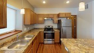 This single-floor residence offers a functional and comfortable layout designed for everyday living. The kitchen serves as a standout feature, showcasing warm oak cabinetry, granite-look countertops, stainless steel appliances including a refrigerator, range, and dishwasher, and a central island with pendant lighting overhead. Rich hardwood-style flooring extends through the kitchen and into the open living area, which is brightened by recessed lighting and a window that draws in natural light.

The bedrooms are finished with plush carpeting and neutral tones, providing a calm and restful atmosphere. One bedroom features a walk-in closet with built-in shelving and direct access to an adjacent room, offering added versatility. Windows throughout the bedrooms frame outdoor views and allow for ample daylight.

The bathroom is clean and simply appointed, with a full tub-shower surround, a wood-trimmed vanity, and access to a closet with wire shelving. A dedicated laundry area houses a full-size washer and dryer, adding significant convenience to the home.

Consistent warm wood trim, neutral wall tones, and durable flooring selections tie the space together cohesively, creating a move-in-ready environment that balances practicality with a welcoming residential character.