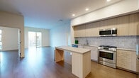 This contemporary single-floor residence showcases a thoughtfully designed open-concept layout, seamlessly connecting the kitchen and living areas. The kitchen is a standout feature, equipped with stainless steel appliances including a gas range, built-in microwave, dishwasher, and a large French-door refrigerator. Light wood cabinetry extends floor-to-ceiling, complemented by a marble-style tile backsplash and a generous center island with a clean, neutral countertop — ideal for both meal preparation and casual dining. Recessed lighting illuminates the space throughout.

Wide-plank hardwood flooring flows consistently across the main living areas and into the bedrooms, lending warmth and visual continuity. The living area benefits from abundant natural light through a full-width sliding glass door that opens to an outdoor balcony, offering views of the surrounding building exterior.

The bedrooms are well-proportioned, featuring hardwood floors, crisp white walls, and sliding doors or windows that connect to outdoor areas. The bathroom is finished with large-format light tile flooring, a wide double-sink vanity with a quartz countertop and warm wood cabinetry, and a backlit wall mirror that enhances the bright, clean aesthetic. The overall ambiance of the residence is modern, minimal, and move-in ready.
