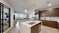 This well-appointed 2-bedroom, 2-bathroom residence is thoughtfully designed across a single floor, offering a seamless blend of modern aesthetics and functional living. The open-concept kitchen and living area serves as the heart of the home, featuring rich dark-walnut cabinetry, a large quartz-topped island with an undermount sink and pendant lighting, stainless steel appliances, and a tile backsplash. Light wood-style flooring flows throughout, enhancing the bright and airy atmosphere. The living room opens to a private balcony through sliding glass doors, bringing in abundant natural light and outdoor views of lush palm-lined surroundings. Both bedrooms are generously sized, fitted with plush carpeting, ceiling fans, and large windows that frame the tropical exterior scenery. Each bedroom benefits from its own walk-in closet, complete with multi-rod hanging systems and shelving. The bathrooms feature large-format tile flooring, wood-toned vanity cabinetry, and white quartz countertops. A dedicated in-unit laundry room houses a full-sized side-by-side washer and dryer. A hallway connects all rooms efficiently, while two closets provide additional storage throughout the residence.