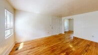 Located at 6415 Newport Ave in Norfolk, Virginia, this two-bedroom, one-bathroom single-floor home offers a practical and well-organized layout. Warm-toned hardwood flooring runs consistently throughout the living areas and bedrooms, lending a cohesive and classic character to the interior. The two living areas provide flexible space for both relaxing and entertaining, connected by a central hallway that facilitates easy movement throughout the home. The primary bedroom is generously sized, featuring dual windows that invite an abundance of natural light and views of the surrounding greenery. The second bedroom also includes a window with outdoor views and a ceiling light fixture. Both bedrooms offer closet access. The kitchen is equipped with warm oak cabinetry, granite-look countertops, a stainless steel sink, and a white electric range, all complemented by light vinyl flooring and a window providing natural light. The bathroom retains a vintage aesthetic with cream and black tile detailing, a full-size soaking tub, and a window for ventilation and light. Throughout the home, white walls and trim create a clean, neutral backdrop, while natural light flowing through multiple windows enhances the overall brightness and openness of the space.