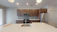 Located at 12 W Gay St in the heart of downtown Columbus, Ohio, this single-floor unit offers a sleek, modern design with thoughtful finishes throughout. The open-concept kitchen is a standout feature, showcasing rich walnut-toned cabinetry with bar-pull hardware, crisp white quartz countertops, a subway tile backsplash, and a full suite of stainless steel appliances including a range, over-the-range microwave, and refrigerator. A generously sized kitchen island with an undermount sink and pendant lighting above serves as both a functional workspace and a natural gathering point. Light wood-tone flooring runs throughout the main living areas, complementing the neutral color palette and recessed lighting that keeps the space feeling bright and airy. A glass-paned door offers access to an outdoor area, allowing natural light to fill the kitchen and living space. The bedroom is well-proportioned with a large window framing views of the surrounding cityscape, and connects to a spacious walk-in closet outfitted with wire shelving and carpeted flooring for added comfort. The bathroom features a warm wood vanity with quartz countertop, a wide framed mirror, contemporary brushed nickel fixtures, and a full soaking tub with tiled surround. Clean lines and a cohesive modern aesthetic define this well-appointed downtown Columbus residence.