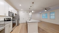 Located in Spring Hill, Tennessee, this single-story, three-bedroom, two-bathroom home offers a clean, modern design with a bright and cohesive aesthetic throughout. The open-concept layout connects the kitchen and living room, creating a spacious, functional common area ideal for both everyday living and entertaining. The kitchen is a standout feature, centered around a large island with a granite countertop, undermount sink, and stylish pendant lighting. White shaker-style cabinetry lines the walls, complemented by stainless steel appliances including a refrigerator, range, and microwave. Light-toned wood flooring flows consistently throughout the entire home, contributing to the airy, unified feel. The living room is generously sized with multiple windows that allow abundant natural light, a ceiling fan, and direct access to an exterior door. Each of the three bedrooms is well-proportioned, featuring large windows with blinds and the same continuous wood flooring. The primary bedroom includes a dedicated walk-in closet with wire shelving and an en-suite bathroom with granite countertops and a walk-in shower. An additional closet with wire shelving provides extra storage. The home's neutral white palette and consistent finishes create a clean, move-in-ready environment throughout.