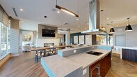 Located at 4900 Seminary Rd in Alexandria, Virginia, this contemporary single-floor amenity space is thoughtfully designed to serve as a dynamic social hub. The open-concept layout seamlessly connects a fully equipped kitchen, communal dining area, lounge, and game room, creating a versatile environment for gathering and entertainment.

The kitchen is a standout feature, showcasing a large stone-topped island with bar seating, rich wood cabinetry, a bold teal geometric tile backsplash, stainless steel appliances, and a statement overhead range hood. Dramatic pendant lighting adds a polished, modern touch.

The dining area centers on a live-edge wood communal table surrounded by classic wishbone chairs, with a sleek linear fireplace and wall-mounted television serving as the focal point. Herringbone-patterned hardwood flooring flows throughout, lending warmth and texture to the space.

Floor-to-ceiling glass walls and doors flood the lounge area with natural light and provide direct views of and access to an outdoor terrace. Comfortable seating arrangements make this a welcoming retreat. The game room offers a full-size shuffleboard table, foosball table, and additional seating, set against a deep teal patterned accent wall. Curated artwork is displayed throughout, enhancing the space's refined, contemporary character.