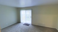 This two-floor residential space offers a straightforward and functional layout designed for comfortable everyday living. The main living area is finished with wall-to-wall carpeting, providing a soft and warm underfoot feel throughout. A prominent sliding glass door floods the room with natural light and offers a direct view of the surrounding greenery outside, creating a seamless connection between the interior and the outdoors. Vertical blinds are fitted to the sliding door, allowing for easy light and privacy control. The walls are finished in a clean, neutral tone that lends the space a calm and open atmosphere. Clean white baseboards frame the carpeted floors, adding a crisp, finished look to the room. The overall ambiance is understated and move-in ready, with a simple aesthetic that provides a versatile backdrop for a variety of interior styles. Spanning two floors, the space offers separation between living and private areas, making it well-suited for those seeking a clear distinction between communal and personal spaces. The abundance of natural light, neutral finishes, and access to outdoor views are standout characteristics that contribute to the overall livability of this residence.