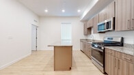 This single-floor residence showcases a thoughtfully designed, contemporary layout with consistent light wood-tone flooring throughout the main living areas. The kitchen serves as a central highlight, featuring a large island with granite countertops, matching granite along the perimeter counters, and sleek flat-front cabinetry in a warm wood finish. Stainless steel appliances include a gas range, built-in microwave, dishwasher, and a French door refrigerator with an ice dispenser, providing a fully functional cooking environment.

The open layout extends into a generously sized living area illuminated by recessed lighting and natural light from a tall, narrow window. A dedicated laundry alcove with a stacked washer and dryer unit offers added convenience, while a ceiling fan enhances comfort throughout the living space.

The bathroom is appointed with granite countertops, an undermount sink, wood-toned cabinetry, and a full tub-shower combination. The bedroom features plush carpeting, a tray ceiling with a ceiling fan, a large window, and a sliding glass door opening to a private balcony with expansive mountain and pool views, creating a bright and serene retreat.