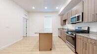 This single-floor residence showcases a thoughtfully designed, contemporary layout with consistent light wood-tone flooring throughout the main living areas. The kitchen serves as a central highlight, featuring a large island with granite countertops, matching granite along the perimeter counters, and sleek flat-front cabinetry in a warm wood finish. Stainless steel appliances include a gas range, built-in microwave, dishwasher, and a French door refrigerator with an ice dispenser, providing a fully functional cooking environment.

The open layout extends into a generously sized living area illuminated by recessed lighting and natural light from a tall, narrow window. A dedicated laundry alcove with a stacked washer and dryer unit offers added convenience, while a ceiling fan enhances comfort throughout the living space.

The bathroom is appointed with granite countertops, an undermount sink, wood-toned cabinetry, and a full tub-shower combination. The bedroom features plush carpeting, a tray ceiling with a ceiling fan, a large window, and a sliding glass door opening to a private balcony with expansive mountain and pool views, creating a bright and serene retreat.