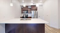 This thoughtfully designed one-bedroom, one-bathroom unit in South Ogden, Utah offers a comfortable and functional living experience across a single floor. The open-concept kitchen and living area forms the heart of the home, featuring wood-look luxury vinyl plank flooring, a ceiling fan with light fixture, and a sliding glass door that floods the space with natural light and provides outdoor access. The kitchen is outfitted with rich dark-stained cabinetry, stainless steel appliances including a refrigerator and gas range, a built-in microwave, and a spacious kitchen island with a double-basin sink and pendant lighting overhead — ideal for both meal prep and casual dining. The bedroom offers soft carpeting, a window with outdoor views, and generous wall space. A standout architectural detail is the board-and-batten wainscoting accent wall, adding a refined touch to the interior. The full bathroom features wood-look flooring, a dark-stained vanity with a light countertop, and a shower-tub combination. A dedicated laundry room with full-size washer and dryer units, built-in shelving, and additional storage rounds out this efficient and well-equipped home.