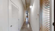 Located in the Americus 8 building in Memphis, TN, this 2-bedroom, 2-bathroom loft-style residence showcases an industrial-chic aesthetic defined by polished concrete floors, exposed concrete columns, visible overhead ductwork, and soaring ceilings that create a striking sense of volume throughout. The open-plan living, dining, and kitchen area serves as the heart of the unit, where floor-to-ceiling industrial-pane windows flood the space with natural light and frame urban views. The kitchen features granite countertops, white cabinetry with under-cabinet lighting, and a full suite of appliances. A long hallway with wall-mounted gooseneck sconces connects the bedrooms, each offering generous proportions and walk-in closets outfitted with wire shelving systems. The bathrooms are finished with granite-topped vanities and white cabinetry. An in-unit laundry room houses a full-size washer and dryer. Additional highlights include a balcony and a patio, providing outdoor living options. The combination of raw architectural elements—exposed brick accents, concrete columns, and open ceilings—with clean white walls and modern finishes gives this residence a distinctive urban character well-suited to contemporary living in Memphis.