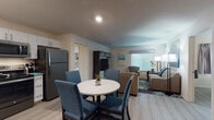 Located at 1525 W Arrowood Rd in Charlotte, NC, this single-floor suite offers a thoughtfully designed layout ideal for extended stays or comfortable living. The open-concept living and dining area is anchored by light wood-style flooring throughout, a round dining table with four blue upholstered chairs, and a cozy living room furnished with neutral-toned sofas and accent artwork. A flat-screen TV and media console complete the lounge area, which benefits from natural light through large windows with blinds.

The fully equipped kitchen features white cabinetry with granite-style countertops, stainless steel appliances including a refrigerator, range, microwave, and dishwasher — offering everything needed for home-style cooking. Each of the two bedrooms provides a comfortable retreat, with king-size beds, coordinating artwork, wall-mounted televisions, and open wire-rack closets offering ample storage space. Both bedrooms are brightened by windows with curtains.

The suite includes two bathrooms: one with a glass-enclosed shower and another with a full soaking tub and shower combination. Both bathrooms feature granite-topped white vanities and wood-look flooring. A stacked washer and dryer is also included within the unit, adding everyday convenience to this well-rounded Charlotte suite.