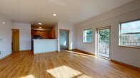 This thoughtfully designed single-floor residence offers a clean, modern aesthetic throughout. The open-concept living and dining area is bathed in natural light from large windows and a sliding glass door that leads to a private balcony overlooking lush, mature trees. Warm honey-toned hardwood flooring flows seamlessly across the main living spaces, complemented by crisp white walls and recessed lighting.

The kitchen is well-appointed with warm wood cabinetry, white countertops, and a full suite of stainless steel appliances including a refrigerator, range, over-the-range microwave, and dishwasher. A peninsula counter separates the kitchen from the living area, providing both additional workspace and a natural visual boundary.

The bedrooms are carpeted for comfort, each featuring large sliding windows that frame serene outdoor views of trees and open sky. One bedroom includes a closet with built-in shelving. A hallway lined with wood-trimmed doors connects the private areas of the unit.

The bathroom features tile flooring, warm wood cabinetry with a white countertop vanity, a wall-mounted mirror, and a full-size soaking tub with a tub/shower combination. Clean lines and neutral finishes throughout create a cohesive, move-in ready space.