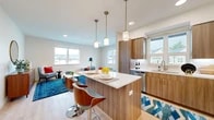 Located at 10999 SE 37th Ave in Portland, Oregon, this well-designed 2-bedroom, 2-bathroom single-floor residence offers a thoughtful layout with modern finishes throughout. The open-concept kitchen and living area serves as the heart of the home, where warm wood-toned cabinetry, quartz countertops, and a central island with pendant lighting create an inviting and functional space. Stainless steel appliances, including a full-size refrigerator, dishwasher, and range, complete the kitchen. Light hardwood-style flooring flows throughout the main living areas, enhancing the bright, airy atmosphere created by multiple large windows. The living room offers ample natural light and neighborhood views. Both bathrooms feature clean, contemporary design with wood-finish vanities, full soaking tubs, and crisp white fixtures. The primary bedroom is a comfortable retreat with a walk-in closet, while the second bedroom features its own large window with outdoor views and plush carpeting. A hallway with recessed lighting connects the rooms, accented by clean white walls. The overall aesthetic is modern and cohesive, blending warm wood tones with neutral palettes for a welcoming, move-in-ready feel.