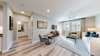 This well-designed single-story residence offers a bright and contemporary living experience across a thoughtfully arranged floor plan. The open-concept living and dining area is anchored by light wood-look flooring, recessed lighting, and large windows that fill the space with natural light. A ceiling fan adds comfort, while wall art and a mounted flat-screen TV give the area a polished, curated feel. The dining nook accommodates a bistro-style table with upholstered chairs, positioned conveniently adjacent to the living space.

The kitchen is a standout feature, showcasing white shaker-style cabinetry extending to the ceiling, a classic subway tile backsplash, dark countertops, and a full suite of stainless steel appliances including a French door refrigerator, range, microwave, and dishwasher. A kitchen island with bar seating provides additional prep and casual dining space.

Two bedrooms offer comfortable retreats; one features soft neutral tones with plush carpeting and natural light, while the second bedroom makes a bold statement with a deep blue accent wall and woven wall art. Both rooms include ceiling fans and window treatments. The bathroom is clean and functional, with a wide vanity, dark countertop, large mirror, wood-look flooring, and a shower-tub combination.