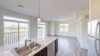 This well-appointed single-floor residence showcases a thoughtfully designed open-concept layout that seamlessly connects the kitchen, dining, and living areas. The kitchen is a standout feature, equipped with stainless steel appliances including a refrigerator, range, and built-in microwave, all complemented by rich dark espresso cabinetry, light quartz countertops, and a central island with a sink and pendant lighting overhead. Wood-look luxury vinyl plank flooring extends throughout the main living areas, adding warmth and continuity to the space.

The living area is bathed in natural light through large windows and provides direct access to a private balcony overlooking open green surroundings. The bedrooms are generously proportioned, featuring plush carpeting and oversized windows that frame views of the landscape and nearby streetscapes, allowing abundant daylight to fill each room.

Two bathrooms serve the residence: a full bathroom featuring a walk-in shower, wide vanity with white cabinetry, quartz countertops, and tile flooring, and a second bathroom with a clean, functional design. Neutral tones in warm beige and white are used throughout, creating a bright and cohesive aesthetic. The overall ambiance is clean, modern, and move-in ready.