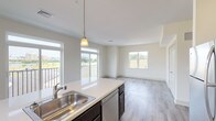 This well-appointed single-floor residence showcases a thoughtfully designed open-concept layout that seamlessly connects the kitchen, dining, and living areas. The kitchen is a standout feature, equipped with stainless steel appliances including a refrigerator, range, and built-in microwave, all complemented by rich dark espresso cabinetry, light quartz countertops, and a central island with a sink and pendant lighting overhead. Wood-look luxury vinyl plank flooring extends throughout the main living areas, adding warmth and continuity to the space.

The living area is bathed in natural light through large windows and provides direct access to a private balcony overlooking open green surroundings. The bedrooms are generously proportioned, featuring plush carpeting and oversized windows that frame views of the landscape and nearby streetscapes, allowing abundant daylight to fill each room.

Two bathrooms serve the residence: a full bathroom featuring a walk-in shower, wide vanity with white cabinetry, quartz countertops, and tile flooring, and a second bathroom with a clean, functional design. Neutral tones in warm beige and white are used throughout, creating a bright and cohesive aesthetic. The overall ambiance is clean, modern, and move-in ready.