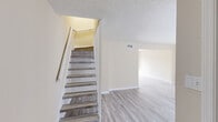 This two-story townhouse in Slidell, Louisiana, offers a clean, neutral interior designed for comfortable everyday living. Light wood-look luxury vinyl flooring runs throughout the home, complementing warm beige walls and bright white trim and baseboards. Textured ceilings add a classic touch consistent across all rooms.

The main level features an open living area that connects to a functional kitchen via a pass-through counter. The kitchen is equipped with white cabinetry, a white electric range, a built-in sink, and a window that brings in natural light. The layout allows for easy interaction between the kitchen and living spaces.

A staircase with wood-toned treads and a white railing leads to the upper level, where the three bedrooms are located. Each bedroom features the same light flooring, ceiling fans with light fixtures, and windows fitted with horizontal blinds that provide views of surrounding greenery. The rooms are well-proportioned and versatile in use.

The two bathrooms are finished in crisp white, with one featuring a soaking tub and shower combination and the other offering a stand-up shower with built-in shelving. Both are efficiently designed and neatly appointed throughout.