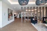 Located at 123 Civitas in Cape Coral, Florida, this thoughtfully designed community amenity space offers an expansive single-floor layout filled with contemporary flair and versatile functionality. The open-plan main area makes a striking first impression with light oak hardwood flooring laid in an elegant herringbone pattern, tall structural columns with a distressed metal finish, and eye-catching woven pendant light fixtures that add a coastal, artistic touch. Large-format abstract artwork adorns the crisp white walls throughout, reinforcing the space's sophisticated aesthetic.

The lounge areas are appointed with navy patterned armchairs, leather seating, and warm wood beam ceilings, centered around flat-screen televisions and a bold navy fluted accent wall. A billiards table anchors a central game area, while a dedicated kitchenette features sleek blue cabinetry, stone countertops, and a distinctive scalloped white tile backsplash. A well-lit conference and meeting room provides flexible seating arrangements with mobile tables and chairs, cove lighting, and curated blue abstract artwork. Recessed and cove lighting throughout creates a warm, welcoming ambiance suited for both social gatherings and productive meetings.
