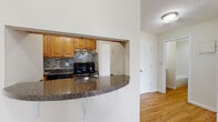 Located at 135 Ward in Revere, Massachusetts, this single-floor residence offers a well-designed layout with a cohesive blend of functional spaces and comfortable finishes throughout. The entryway opens onto warm hardwood-style flooring that extends through the main corridor and into the kitchen area. The kitchen is thoughtfully appointed with warm-toned wood cabinetry, a mosaic tile backsplash, dark granite countertops, and stainless steel appliances including a range and dishwasher. A curved breakfast bar peninsula with metal supports provides additional counter space and creates a natural connection to the adjacent living area. The spacious living room features soft wall-to-wall carpeting, clean white walls, and a large sliding glass door fitted with vertical blinds that invites natural light and provides access to an outdoor view. A wall-mounted air conditioning unit serves the space, complemented by baseboard heating found throughout the unit. The bedroom is generously sized with plush carpeting, baseboard heating, and a closet with paneled doors offering ample storage. The bathroom is finished with hardwood-style flooring, a wood-toned vanity with a white countertop, a full bathtub and shower enclosure, and clean, bright fixtures. The overall ambiance of the space is calm and practical, with neutral tones and consistent finishes creating a move-in ready environment.