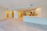 This thoughtfully designed single-floor residence showcases a clean, contemporary aesthetic throughout. The open-concept living and kitchen area is anchored by large floor-to-ceiling windows that frame lush greenery views and flood the space with natural light. Light-toned large-format tile flooring runs seamlessly throughout, reinforcing the bright, airy ambiance.

The kitchen is a standout feature, outfitted with crisp white shaker cabinetry adorned with brushed gold hardware, a white quartz peninsula and countertops, a tiled backsplash, and a full suite of stainless steel appliances including a refrigerator, range, microwave, and dishwasher. Recessed lighting ensures the space is well-lit at all hours.

The bedrooms are generously proportioned with clean white walls and ample natural light, including one room with a tall window offering a tranquil outdoor view. Each room connects conveniently to the well-appointed bathrooms. The bathrooms feature white vanities with gold fixtures, a circular gold-framed mirror, white quartz countertops, and a beautifully tiled walk-in shower with a sleek sliding glass door. The overall design is cohesive and modern, with gold accents serving as a unifying design element across the kitchen and bathrooms, lending an elevated, refined character to the entire residence.