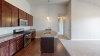 Located at 1711 Lake Superior Rd in Valparaiso, Indiana, this well-appointed 2-bedroom, 1-bathroom residence offers a thoughtfully designed single-floor layout with a clean, neutral aesthetic throughout. The standout kitchen features rich dark wood cabinetry, granite countertops, stainless steel appliances including a gas range, microwave, and refrigerator, and a curved peninsula island with an undermount sink — all beneath impressively soaring ceilings with pendant lighting and durable hardwood-style flooring. The kitchen flows openly toward the hallway, connecting seamlessly to the rest of the home. Both bedrooms are carpeted and finished with warm neutral tones, offering natural light through large windows fitted with horizontal blinds that frame views of the surrounding greenery. The primary bedroom provides a generous, comfortable footprint. The full bathroom continues the home's design consistency with dark wood vanity cabinetry, granite countertops, a large mirror, and hardwood-style flooring. A dedicated closet and two hallways round out the functional layout. A private balcony extends the living space outdoors, offering open views of lush trees and landscaped grounds beneath an expansive sky — a serene retreat within this well-kept Valparaiso community.