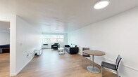 This efficiently designed 1-bedroom, 1-bathroom unit offers a thoughtful layout across a single floor, making excellent use of its compact footprint. The open living area is bright and airy, featuring warm light wood flooring, white walls, and a large window that invites natural light and provides views of the surrounding neighborhood. The living space comfortably accommodates a seating area and a dining table, creating a versatile environment for both relaxing and entertaining.

The kitchen is outfitted with stainless steel appliances — including a full-size refrigerator, gas range, and microwave — complemented by white shaker-style cabinetry and clean countertops, offering a functional and modern cooking space.

The bedroom is a well-sized private retreat, featuring the same light hardwood flooring, a window for natural light, and a built-in sliding-door closet with integrated shelving, providing ample storage. A dedicated desk area makes the room suitable for work or study as well.

The bathroom features a classic tiled tub-shower combination with distinctive mint-green wall tile, a white vanity, and hardwood flooring, lending a clean retro aesthetic. Throughout the unit, the consistent use of light wood flooring, neutral white walls, and flush-mount lighting creates a cohesive, clean, and modern atmosphere.