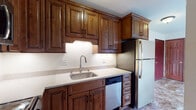 This single-floor unit offers a practical and comfortable layout across several well-defined living spaces. The kitchen serves as a functional centerpiece, showcasing rich, dark-stained wood cabinetry with raised-panel detailing and under-cabinet lighting that illuminates light-toned countertops. Stainless steel appliances—including a gas range, built-in microwave, dishwasher, and refrigerator—provide a full suite of modern conveniences. A stainless steel undermount sink with a pull-down faucet completes the workspace.

The living and entry areas transition between tile flooring near the front door and plush carpeting throughout the main living spaces, creating a warm and inviting atmosphere. A ceiling-mounted light fixture and neutral white walls keep the entryway bright and welcoming.

The bedrooms are carpeted and feature ceiling fans with light kits, baseboard heating, and windows that allow natural light and outdoor views. One bedroom also includes a wall-mounted air conditioning unit for added climate control.

The bathroom features large-format stone-look ceramic wall tiles surrounding a full soaking tub with a handheld showerhead. A wood-toned vanity cabinet with a white basin sink and chrome hardware completes the space with a clean, classic aesthetic throughout.