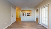 This single-story residence offers a well-organized, open-concept layout finished with consistent light wood-style flooring throughout. The main living area is spacious and airy, framed by crown molding and neutral warm-toned walls that create a welcoming ambiance. A ceiling fan provides additional comfort, and large windows and a glass door allow generous natural light to fill the space while offering outdoor views.

The kitchen is positioned centrally and features a pass-through design with a raised bar, white cabinetry, subway tile backsplash, dark countertops, a gold-toned undermount sink, and a full suite of stainless steel appliances including a refrigerator, electric range, and over-the-range microwave. The layout maximizes functionality with ample counter and storage space along both sides.

The bedroom is comfortably proportioned, also finished with wood-style flooring and a ceiling fan. The bathroom connects to a walk-in closet equipped with built-in shelving, providing practical storage. The bathroom itself features wood-style flooring, clean white fixtures, and a tiled shower area. The entry foyer is defined and leads efficiently into the main living spaces, giving the unit a clear and logical flow throughout.