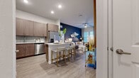Located along LPGA Blvd in Daytona Beach, FL, this well-designed 2-bedroom, 2-bathroom residence offers a contemporary single-floor layout with cohesive modern finishes throughout. The open-concept living and kitchen area serves as the heart of the home, where wood-look plank flooring, recessed lighting, and a striking navy accent wall create an inviting yet sophisticated atmosphere. The living room features soaring ceilings, a ceiling fan, and large windows that flood the space with natural light, alongside access to an outdoor area. The kitchen is outfitted with taupe shaker-style cabinetry, stainless steel appliances, a subway tile backsplash, white quartz countertops, and a peninsula island with bar seating — ideal for casual dining and entertaining. The spacious primary bedroom offers generous natural light through plantation-shuttered windows and connects to a walk-in closet with multi-rail shelving systems. The en-suite primary bathroom features a dual-sink vanity with matching cabinetry, a glass-enclosed shower, and elegant tile flooring. The second bedroom is equally bright and comfortable, with its own accent wall and ample natural light. A hallway connects all rooms efficiently, completing this thoughtfully composed floor plan.