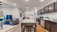 This single-floor residence is thoughtfully designed with a cohesive modern aesthetic throughout. The open-concept kitchen and living area serves as the heart of the home, where rich dark-brown cabinetry with sleek hardware pairs with light granite countertops for a striking contrast. A central kitchen island with bar seating provides additional workspace and casual dining, while stainless steel appliances — including a range, microwave, and dishwasher — complete the functional layout. Light wood-look flooring flows throughout the common areas, adding warmth and continuity.

The living room is bright and inviting, centered around French doors that allow abundant natural light and offer access to the outdoors. A ceiling fan adds comfort to the space. An adjacent flex area with the same flooring provides versatility as a secondary lounge or office space.

The residence includes multiple bedrooms, each finished with plush carpet and neutral tones that create a calm, restful atmosphere. One bedroom features a window with natural light, while the others offer a quiet, cozy feel. The bathrooms are well-appointed with granite-topped dark vanities and wood-look flooring, with one featuring a walk-in shower. An in-unit laundry area adds everyday convenience to this well-rounded home.