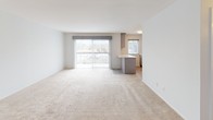 This single-floor studio offers a practical and efficient layout designed to maximize usable space. The open living area is finished with neutral wall-to-wall carpeting and bright white walls, creating a clean, versatile canvas. A large sliding glass door fills the space with natural light while providing outdoor views, complemented by an additional window that further brightens the interior.

The kitchen is thoughtfully updated and separated from the living area by a peninsula with a white countertop, ideal for casual dining or meal prep. Gray shaker-style cabinetry extends to the upper and lower walls, offering generous storage. Black appliances, including a full-size refrigerator, an electric range with oven, and a sleek matte-black faucet over a stainless steel sink, lend a modern contrast to the light countertops. Light tile flooring runs throughout the kitchen area.

The bathroom is well-appointed, featuring a tub and shower combination enclosed by sliding glass doors with marble-style tile surround. Gray floor tile and clean white fixtures contribute to a polished, functional finish. A wall-mounted HVAC unit in the living area ensures year-round comfort throughout this thoughtfully designed studio.