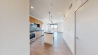 Located at 8150 Rafael Rivera Way in Las Vegas, Nevada, this thoughtfully designed studio offers a contemporary open-concept layout that maximizes every square foot. The combined kitchen and living area forms the heart of the unit, anchored by a central island with a dark countertop and stylish pendant lighting overhead. The kitchen is outfitted with warm wood cabinetry, a blue tile backsplash, stainless steel appliances including a gas range, microwave, refrigerator, and dishwasher, and a sleek undermount sink. Light wood-style flooring runs throughout, lending warmth and continuity across the space. The living area is bathed in natural light streaming through floor-to-ceiling sliding glass doors that open onto a private balcony, offering open views of the surrounding Las Vegas landscape. A ceiling fan keeps the space comfortable year-round. The bathroom features a vessel sink atop a wood-toned vanity with a dark countertop, an illuminated mirror, a soaking tub, and clean white tile walls. A dedicated closet provides practical storage. The unit's crisp white walls and modern finishes create a bright, clean aesthetic throughout.