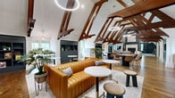 Located at 707 Sanctuary Pl in Charlotte, NC, this expansive single-floor amenity space spans nearly 3,000 square feet of thoughtfully designed communal living. The architecture is immediately striking, defined by soaring vaulted ceilings with richly stained exposed wood truss systems that run throughout, creating a dramatic and cohesive visual identity across every room.

The open-concept dining and living area serves as the heart of the space, featuring warm hardwood flooring, a statement leather sofa in cognac, circular marble-top tables, and ring pendant lighting. A gas fireplace anchors the adjacent living lounge, flanked by built-in dark shelving and framed by plush grid-patterned sofas — perfect for relaxed gatherings.

A dedicated game room offers entertainment with a full-size pool table, ping-pong table, and a wall-mounted TV, all beneath vaulted ceilings with large windows overlooking lush greenery. A coworking nook provides a quieter retreat with warm terracotta walls, marble bistro tables, and wall-mounted desks.

The kitchen area features a marble-topped island, dark wood cabinetry, and an eye-catching botanical mural wallcovering. Natural light pours in through multiple windows throughout, connecting the interior to the surrounding wooded landscape and lending the entire space a welcoming, resort-like ambiance.