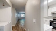 Located in Milwaukie, Oregon, this 2-bedroom, 1-bathroom unit offers a thoughtfully updated interior across a single floor. The open living room serves as the heart of the space, featuring light wood-look luxury vinyl plank flooring, soft gray walls, a ceiling fan with light, and a window that draws in natural light and views of surrounding greenery. The layout flows seamlessly into the kitchen, which has been refreshed with crisp white shaker cabinets, marble-style quartz countertops, stainless steel appliances including a dishwasher, and a window above the sink. An in-unit laundry area is conveniently tucked just off the main living space. Both bedrooms are carpeted with ceiling fans and windows providing natural light; the primary bedroom includes a spacious double-door closet. The bathroom features wood-look LVP flooring, a white vanity with quartz countertop, brushed nickel hardware, and a clean, modern finish throughout. A pet door is visible in the living area and primary bedroom. The exterior includes a shared outdoor area with mature trees providing natural shade, adding a touch of greenery to the surroundings.