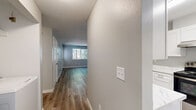Located in Milwaukie, Oregon, this 2-bedroom, 1-bathroom unit offers a thoughtfully updated interior across a single floor. The open living room serves as the heart of the space, featuring light wood-look luxury vinyl plank flooring, soft gray walls, a ceiling fan with light, and a window that draws in natural light and views of surrounding greenery. The layout flows seamlessly into the kitchen, which has been refreshed with crisp white shaker cabinets, marble-style quartz countertops, stainless steel appliances including a dishwasher, and a window above the sink. An in-unit laundry area is conveniently tucked just off the main living space. Both bedrooms are carpeted with ceiling fans and windows providing natural light; the primary bedroom includes a spacious double-door closet. The bathroom features wood-look LVP flooring, a white vanity with quartz countertop, brushed nickel hardware, and a clean, modern finish throughout. A pet door is visible in the living area and primary bedroom. The exterior includes a shared outdoor area with mature trees providing natural shade, adding a touch of greenery to the surroundings.