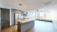 Located in the heart of downtown Dallas on Elm Street, this well-appointed single-floor residence offers 1 bedroom and 2 bathrooms with a thoughtfully designed layout. The open-concept kitchen and living area serves as the centerpiece of the home, featuring warm hardwood flooring, recessed lighting, and a ceiling fan. The kitchen is outfitted with stainless steel appliances including a French door refrigerator, range, microwave, and a wine cooler, complemented by grey cabinetry with glass-front uppers, a white tile backsplash, and a generous island with a quartz countertop and integrated sink. A sliding barn door adds a stylish, modern touch. The living area benefits from dramatic floor-to-ceiling windows that frame sweeping views of the Dallas skyline, filling the space with abundant natural light. The spacious bedroom features plush carpet and connects directly to a well-sized walk-in closet with built-in shelving and hanging rods. The primary bathroom includes large-format tile flooring, a glass-enclosed shower, and a private water closet. A second bathroom provides additional convenience. Neutral tones and dark baseboards and door trim create a clean, contemporary aesthetic throughout.