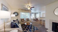 This well-appointed 2-bedroom, 2-bathroom single-floor residence offers a thoughtfully designed open layout that connects the living, dining, and kitchen areas seamlessly. The living room is a welcoming space anchored by a ceiling fan, large windows with blinds and draping curtains that invite abundant natural light, and plush carpeting underfoot. A breakfast bar with bar seating bridges the living area to the galley-style kitchen, which features white cabinetry, light countertops, white appliances including a refrigerator, stove, and dishwasher, and tile flooring that adds a clean, practical finish. The dedicated dining area benefits from multiple windows overlooking greenery, creating a bright and pleasant setting for meals. Both bedrooms are carpeted and feature windows with natural light; one bedroom showcases a bold accent wall in deep navy blue, while the other offers a more neutral, serene palette with ample room for a sitting area. The two bathrooms are finished with tile flooring and white cabinetry; one includes a long vanity with extended counter space, and both feature a shower-tub combination. Throughout the residence, a consistent neutral color palette paired with warm accents creates a cohesive and inviting atmosphere.