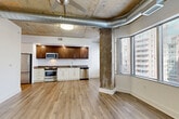 Located at 4501 Ford Ave in Alexandria, VA, this one-bedroom, one-bathroom residence offers a compelling blend of industrial design and contemporary finishes. The open-plan living, dining, and kitchen area serves as the heart of the home, showcasing exposed concrete ceilings with visible ductwork, a ceiling fan, and light wood-style flooring that runs throughout. Large floor-to-ceiling windows flood the space with natural light and frame views of the surrounding Alexandria skyline and greenery, creating an airy, urban atmosphere. The kitchen is well-appointed with dark wood upper cabinetry, stainless steel appliances including a range, microwave, and dishwasher, and a clean white lower cabinet base with ample counter space. Raw concrete structural columns add to the loft-like character of the open living area. The spacious bedroom features the same exposed concrete ceiling aesthetic, a ceiling fan, and wood-style flooring, with generous natural light. The walk-in closet includes built-in adjustable shelving for organized storage. The full bathroom offers a wide dual-sink vanity with white countertops, modern hardware, tile flooring, and a large mirror. A dedicated laundry room, utility room, and hallway with additional closet storage complete this thoughtfully laid-out residence.